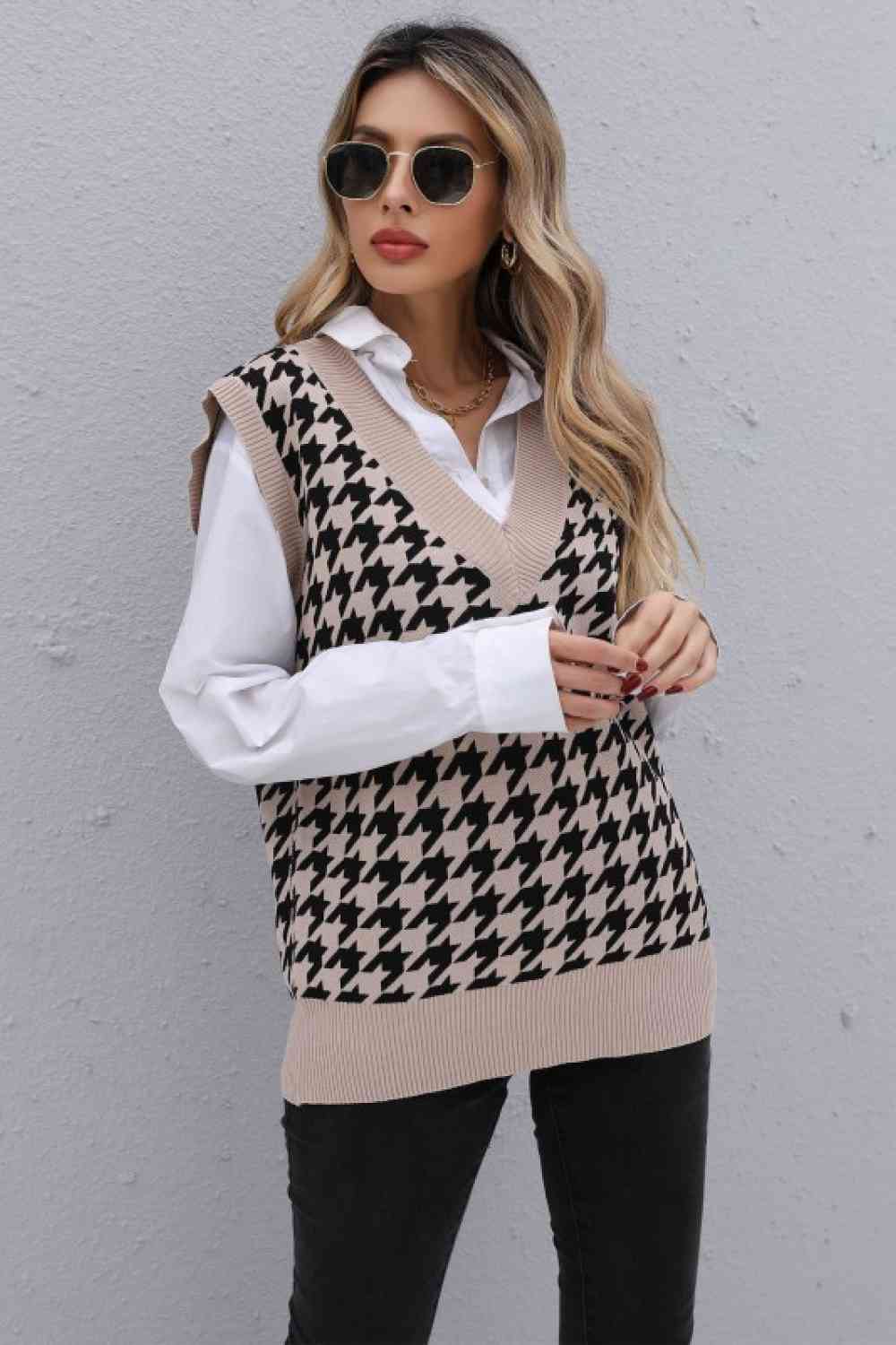 Woman posing in a beige houndstooth sweater vest over a white shirt, with black jeans, sunglasses, and gold hoop earrings.