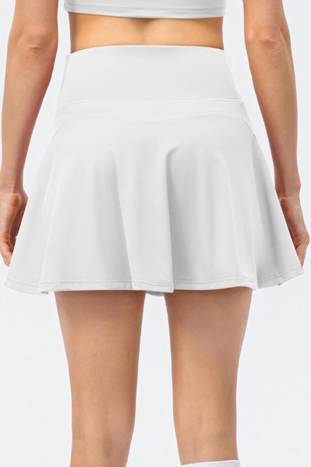 The back view of a model wearing a high-waist active skirt in white, showcasing the wide waistband and flared silhouette.