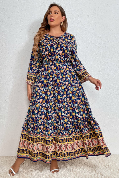 Stylish woman in a floral bohemian dress with intricate border patterns, complemented by sunglasses, set against a white wall and standing on a plush white rug.