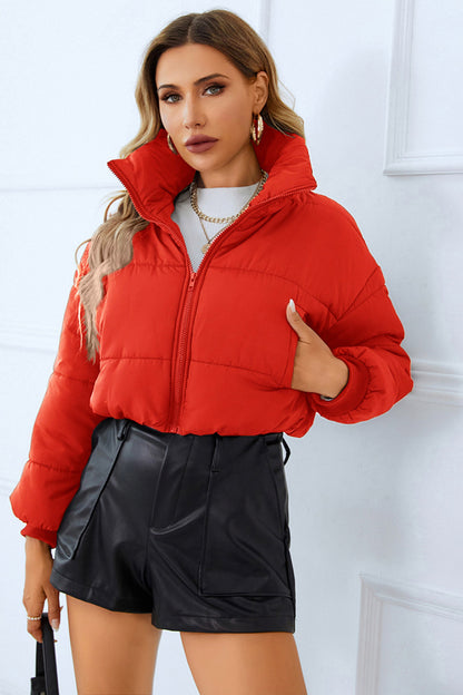 Woman in a red puffer jacket, white sweater, and black leather shorts, paired with gold jewelry, against a white backdrop.