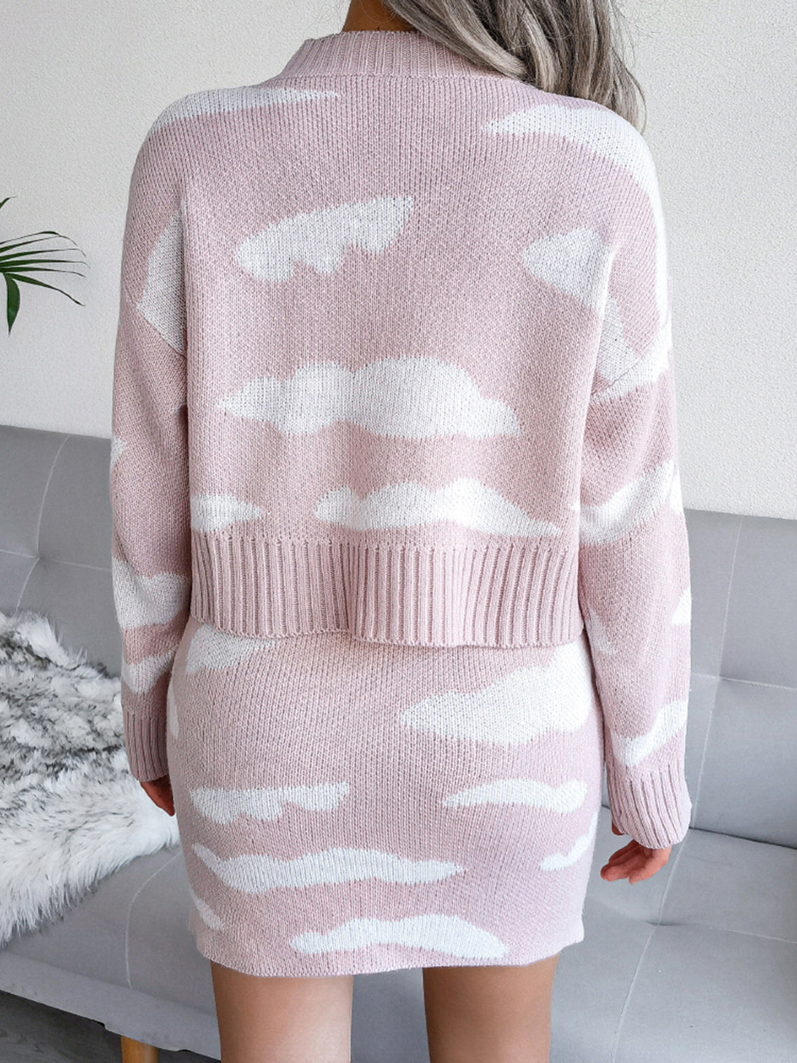 Rear view of a woman wearing a pink sweater dress with white cloud patterns. 