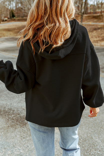 Woman seen from behind wearing a black jacket and light blue jeans set against an outdoor backdrop.