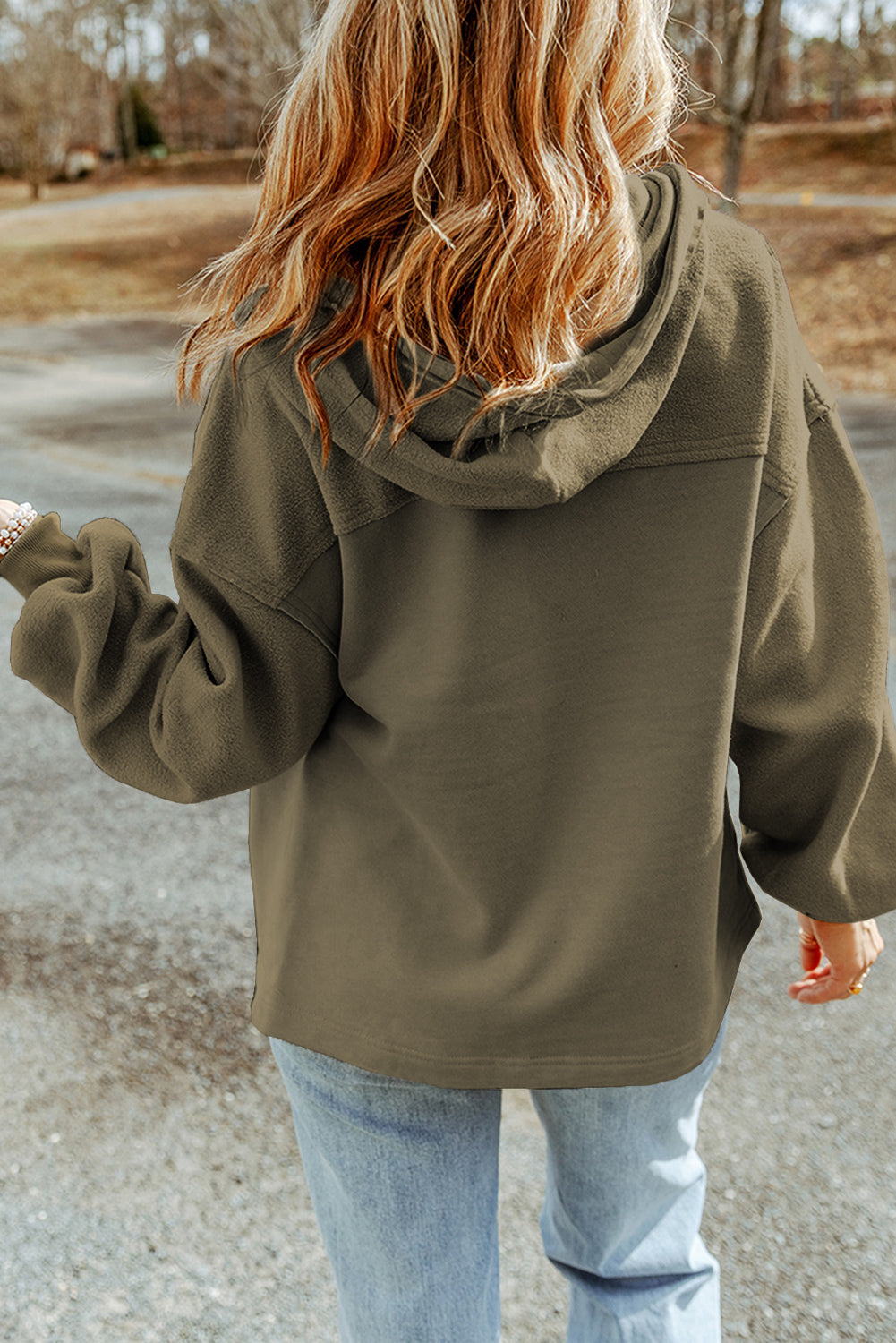 Woman wearing a green jacket and light blue jeans set against an outdoor backdrop.