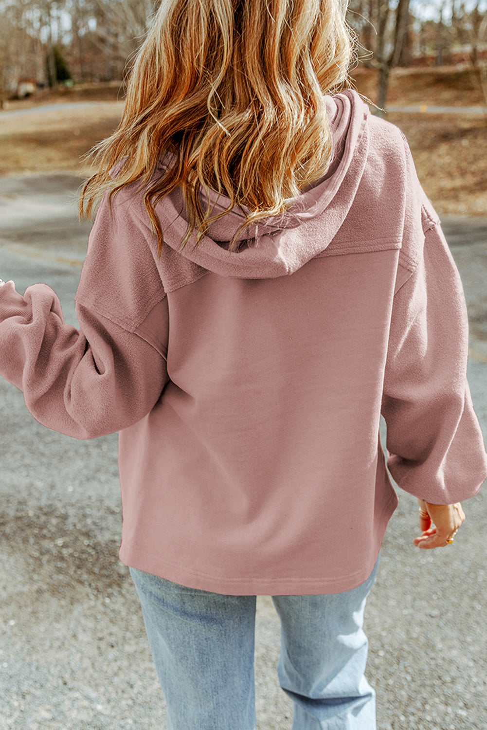 Woman wearing a pink jacket and light blue jeans set against an outdoor backdrop.