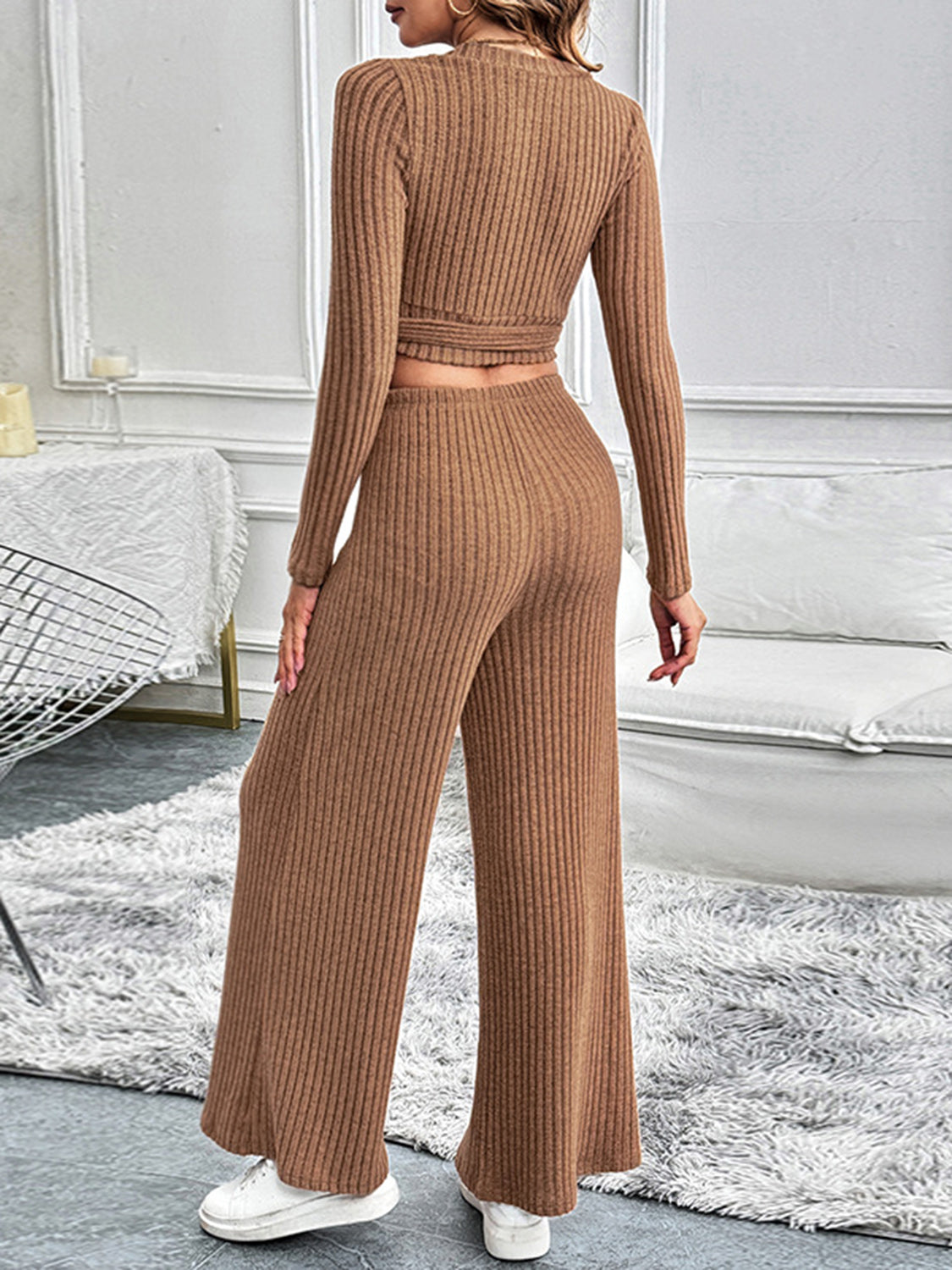 Back view of a model showcasing the camel-colored ribbed knit two-piece lounge set, highlighting the flattering fit and cozy texture of the wrap-style top and high-waisted wide-leg pants.