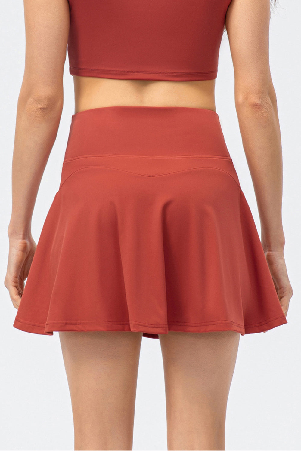 The back view of a model wearing a high-waist active skirt in deep red, showcasing the wide waistband and flared silhouette.