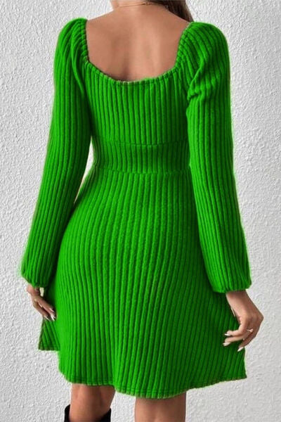 Woman facing away, wearing a ribbed bright green long-sleeve dress with a scooped back, standing against a white textured wall.