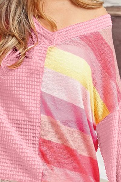 Close-up of a waffle knit sweater with a gradient of pink to yellow tones, the fabric texture is prominent, and part of the wearer's shoulder and hair are visible in the frame.