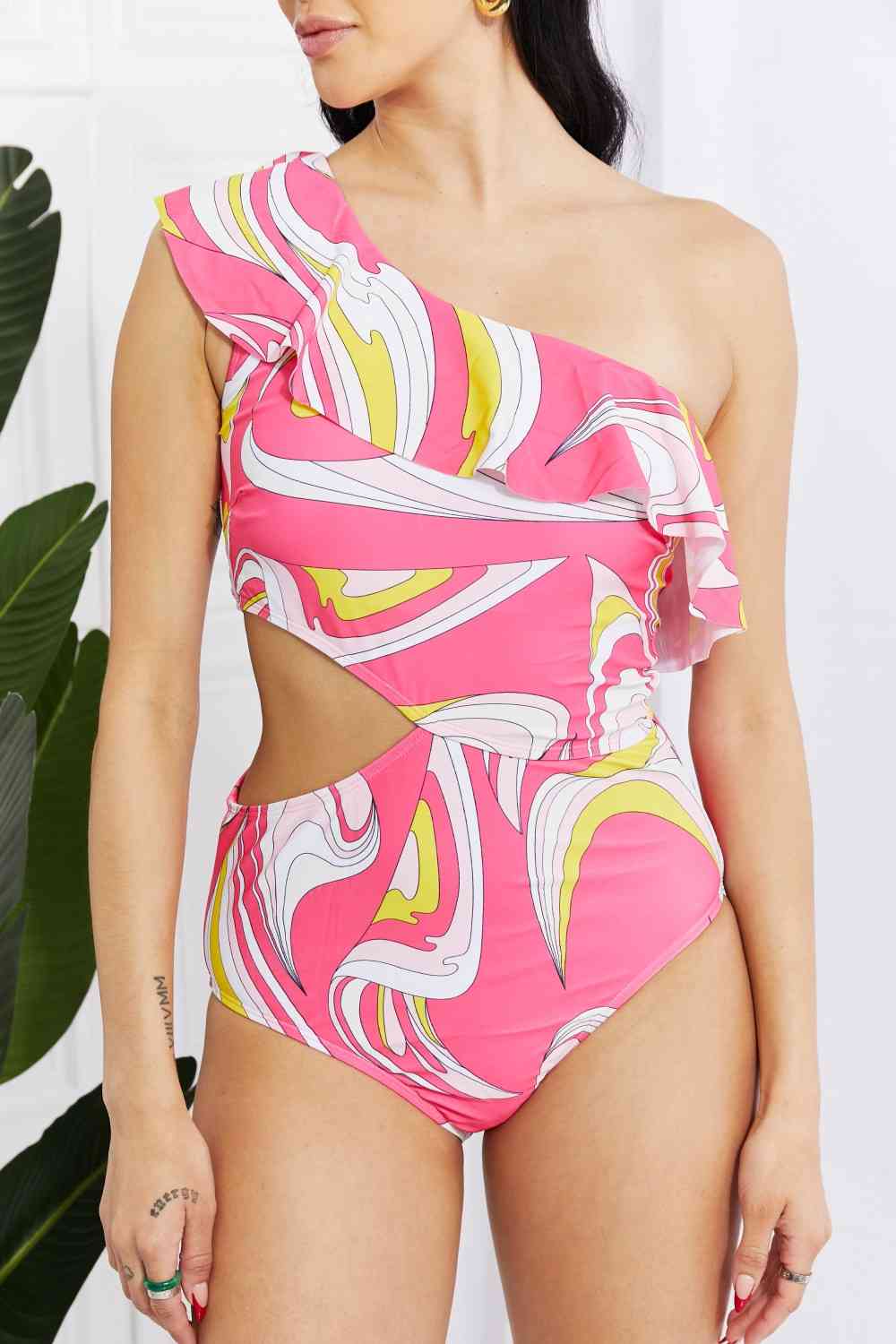 Close-up of pink asymmetric cutout swimsuit with ruffle trim and vibrant swirl pattern, highlighting the one-shoulder design and detailed print.